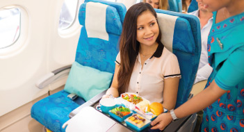 An air hostess serves food to a smiling female passenger