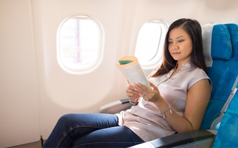 A female passenger stretched out on an extra legroom seat and reading a book