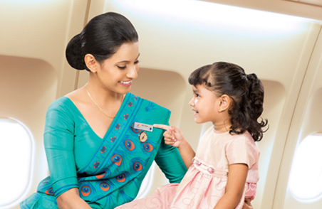 A SriLankan Airlines air hostess holds a smiling girl child pointing at the air hostesses’ name tag