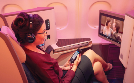 A woman sitting at a business class seat watches a movie on the screen infront of her while smiling